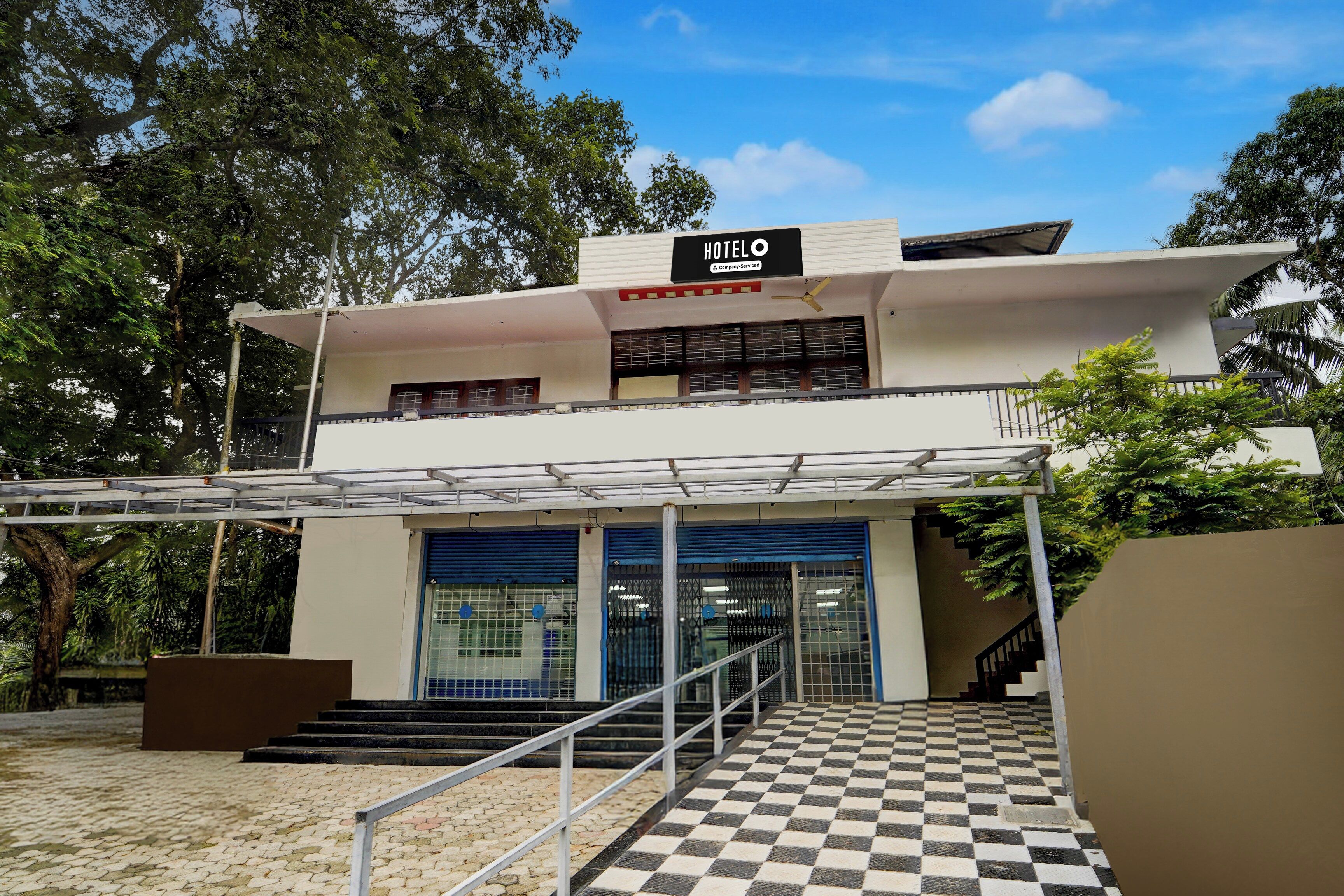 A two-story building with a sign reading 'HOTEL' and a company-serviced logo. There are stairs leading to a gated entrance with a checkered floor pattern.