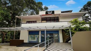 A two-story building with a sign reading 'HOTEL' and a company-serviced logo. There are stairs leading to a gated entrance with a checkered floor pattern.