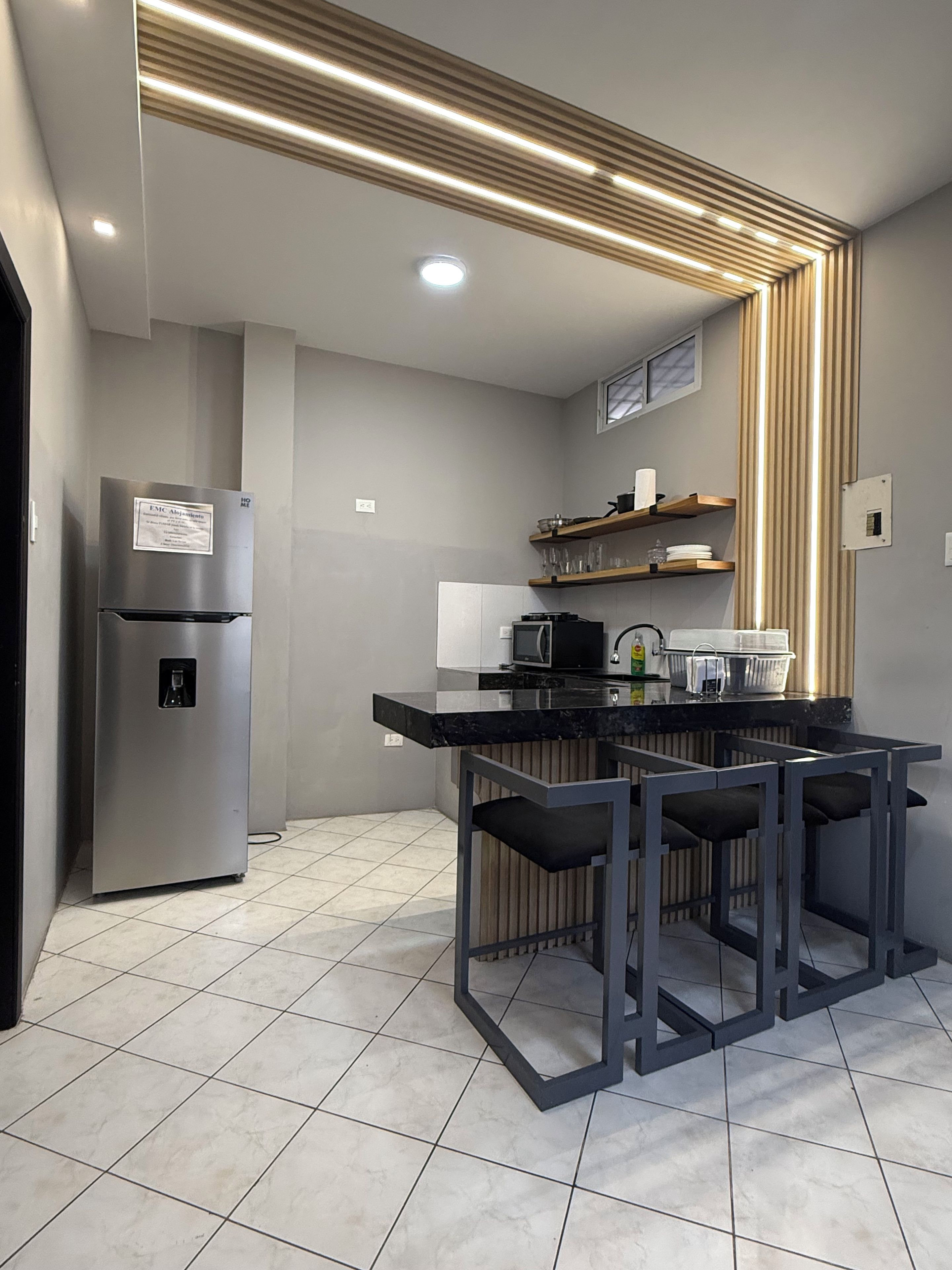 Cozinha moderna com geladeira embutida, micro-ondas e área de jantar com mesa e cadeiras pretas.