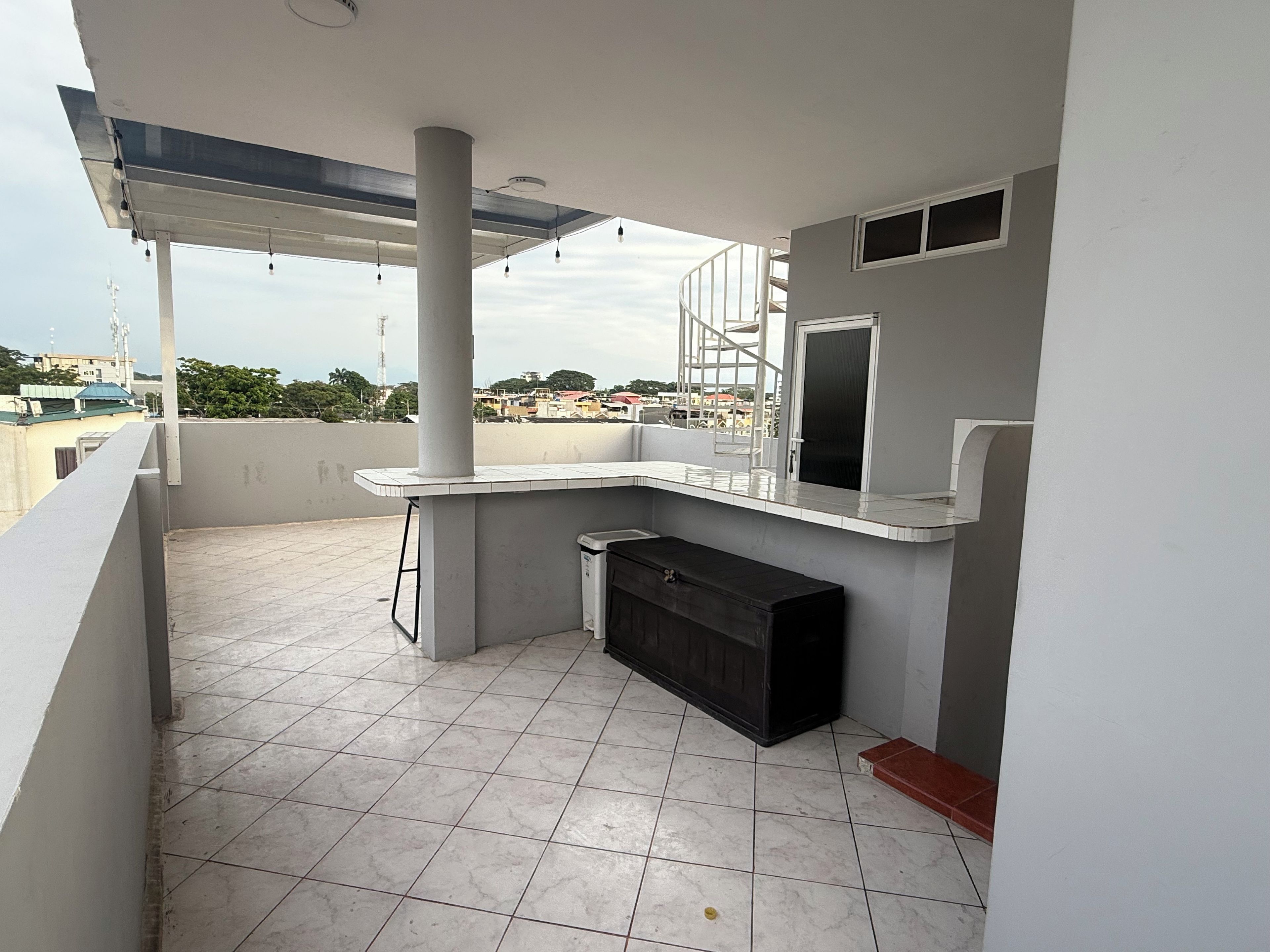 Een balkon met betegelde vloer, een witte kolom, een zwart kastje en een witte balustrade.