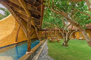 Ein Poolbereich mit Holzterrasse, einer kleinen Brücke und einem Garten mit Bäumen und einem Zaun.