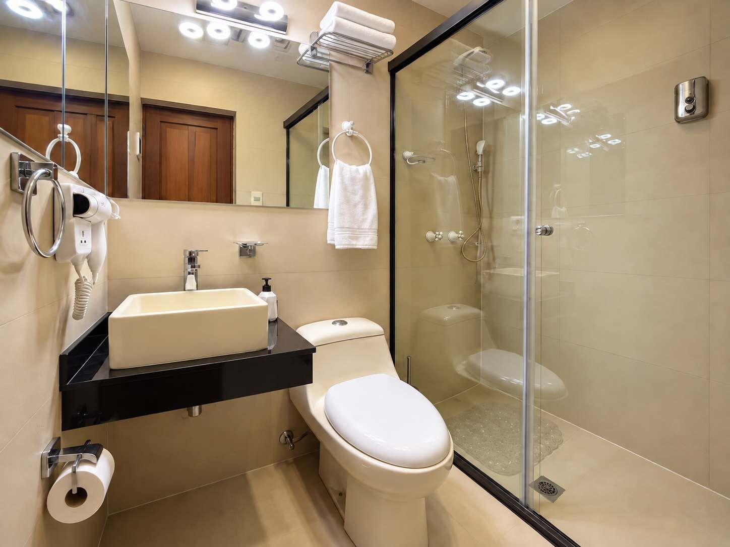A modern bathroom with a glass-enclosed shower, a toilet, a sink, and a hairdryer.