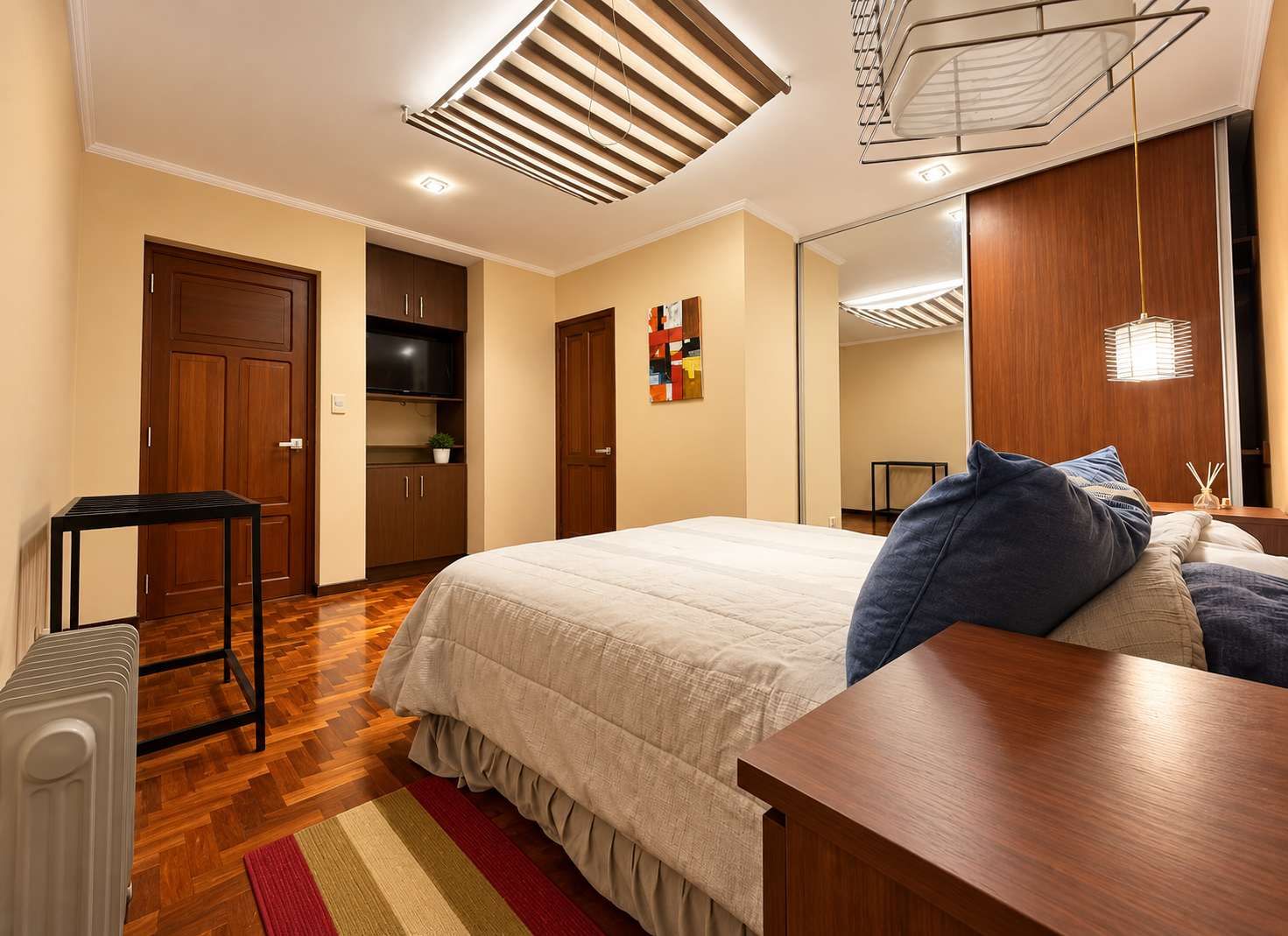 Een slaapkamer met een bed, een houten tafel, een radiator, een televisie en een kledingkast.