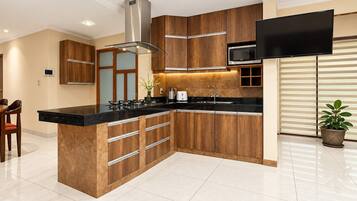 Een moderne keuken met een centraal eiland, houten kastjes, roestvrijstalen apparatuur en een flatscreen televisie die boven het eiland is bevestigd.