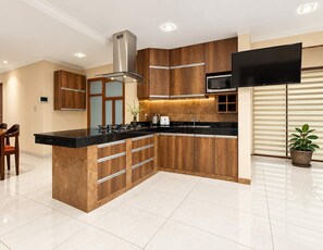 Une cuisine moderne dotée d’un îlot central, de meubles en bois, d’appareils électroménagers en acier inoxydable et d’un téléviseur à écran plat fixé au-dessus de l’îlot.