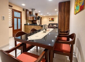Un espace repas moderne avec une table à plateau en verre, des chaises en bois et une cuisine en arrière-plan.