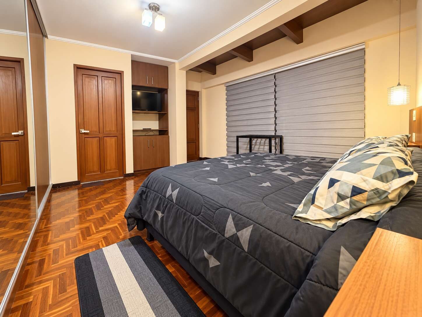 Un dormitorio con cama, armario de madera, televisor integrado y ventana con persianas.