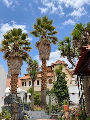 A courtyard with palm trees, a building with a tiled roof, and a stone wall. - Calacoto Suite | Full Bed, Sleeps 2 (La Paz)