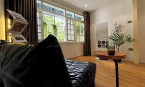 A modern living room with a leather sofa, a round wooden table with a vase, and a large window with curtains. - OH Trendy homes Hoan Kiem LTK - Balcony City VIew (Cua Nam)