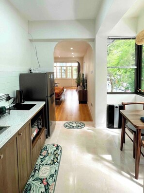 A modern kitchen with a refrigerator, coffee maker, and a dining area with a table and chairs. - OH Trendy homes Hoan Kiem LTK - Balcony City VIew (Cua Nam)