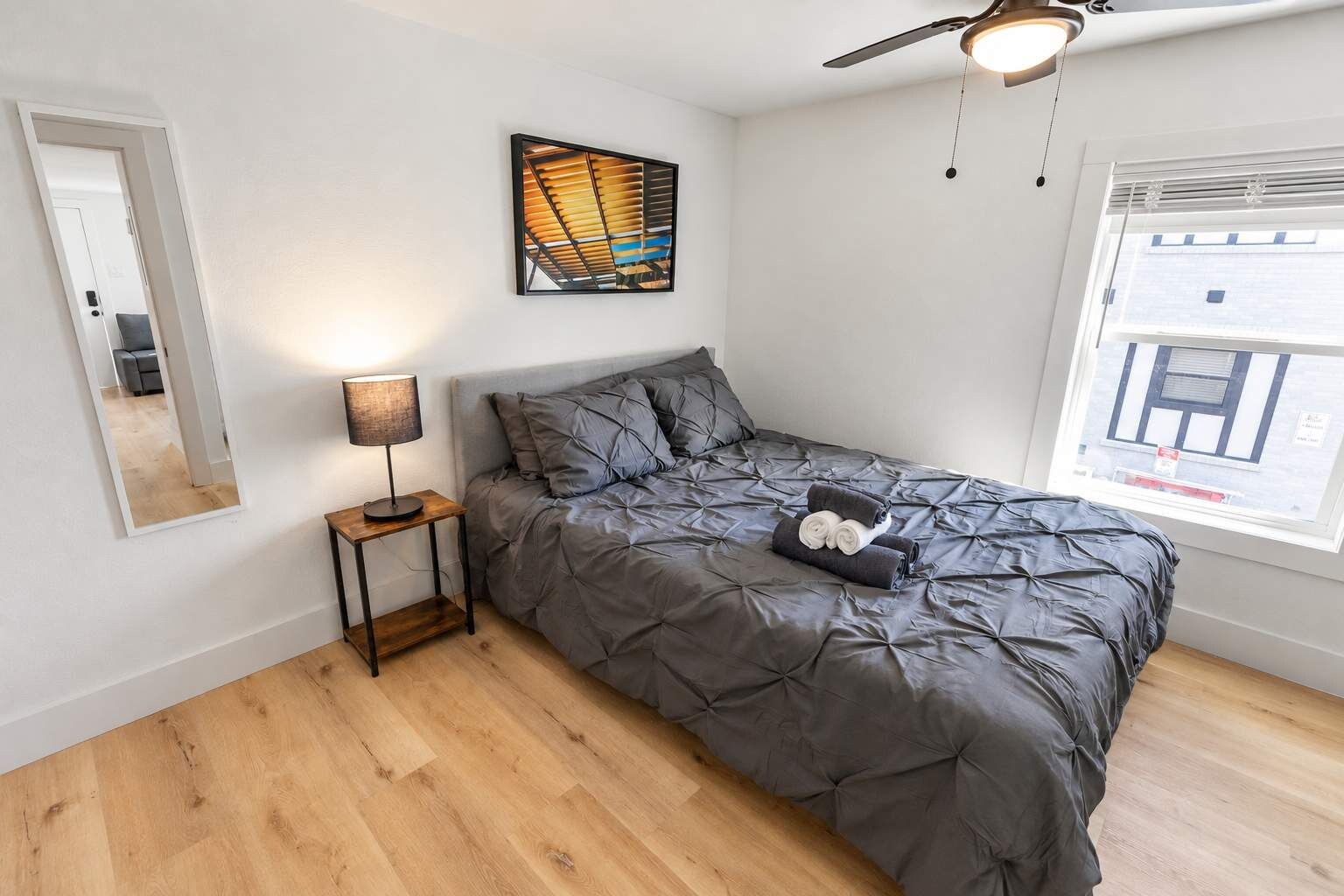 Une chambre à coucher avec un lit, une table de chevet, une lampe, une fenêtre et un ventilateur de plafond.