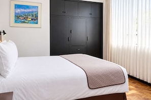 Una habitación de hotel con una cama, un armario, un cuadro y una ventana con cortinas.