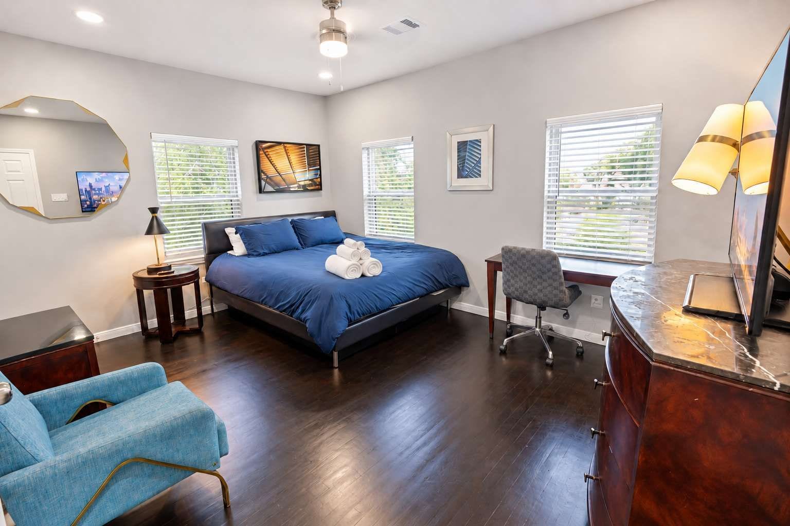 A bedroom with a bed, a desk, a chair, a lamp, and artwork on the walls.