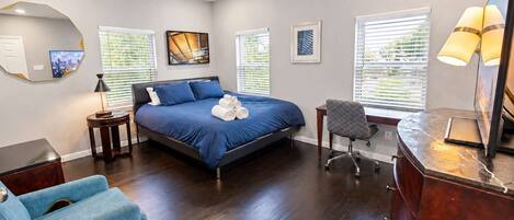 A bedroom with a bed, a desk, a chair, a lamp, and artwork on the walls.