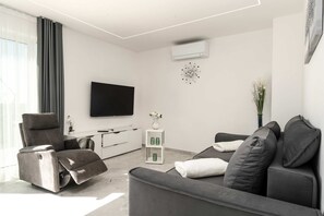 Un salon moderne avec un canapé, un fauteuil inclinable, un téléviseur et un petit meuble blanc.