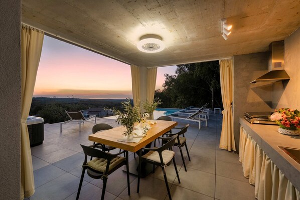Un espace repas offrant une vue sur le coucher de soleil, une piscine et des sièges en plein air.