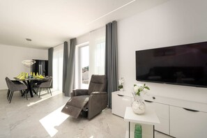 A modern living room with a flat-screen TV, a sofa, a dining area with a table and chairs, and a large window with curtains. - Villa Sanja (100711-K1) - Vizinada (Porec) (Vizinada (Porec))