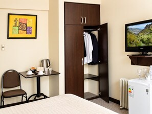 Une chambre d’hôtel comprenant un lit, un bureau avec une bouilloire, une chaise, une armoire, un téléviseur et un radiateur.