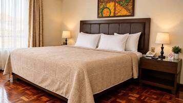 A hotel room with a large bed, wooden flooring, a nightstand with a lamp, and a painting on the wall.