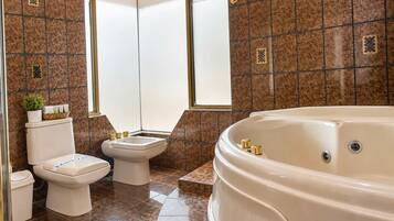 A bathroom with a bathtub, two toilets, and a window.