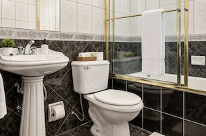 Une salle de bain avec un lavabo sur colonne, des toilettes et une douche séparée par une paroi de verre.
