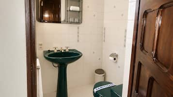 Ein Badezimmer mit einem grünen Waschbecken, einem Spiegel, einer Toilette und einem Mülleimer.