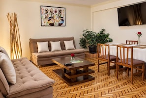 A living room with a sofa, a coffee table, a dining table with chairs, a potted plant, and a painting on the wall.