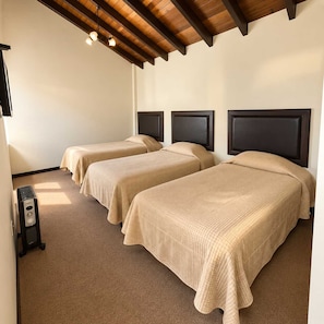 A hotel room with two single beds, a wooden ceiling, and a small heater.