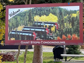 Schild mit der Aufschrift Giant Steps Condominiums, mit Blick auf rote Gebäude und einen Wald.