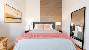 A bedroom with a bed, two bedside tables, a large mirror, a wall-mounted artwork, and a brick wall. - Roami at Studio 135 - Modern and Spacious 2BR (Denver)