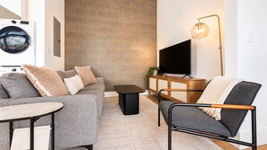 A modern living room with a sofa, armchair, coffee table, and a flat-screen TV. - Roami at Studio 135 - Modern and Spacious 2BR (Denver)