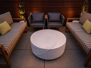 A lounge area with two sofas and a round coffee table, set against a wooden wall with decorative lights. - Roami at Studio 135 - Modern and Spacious 2BR (Denver)