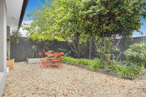 A patio area with a table and chairs, surrounded by gravel and plants.