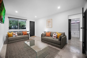 A modern living room with two sofas, a glass coffee table, and a large window.