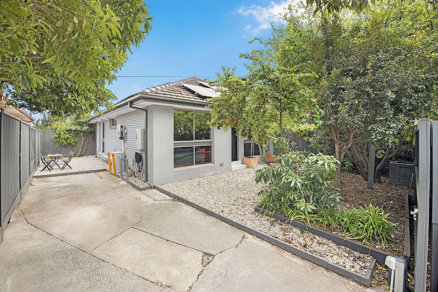 A residential property with a paved driveway, a small patio with outdoor furniture, and a garden area with various plants and trees.
