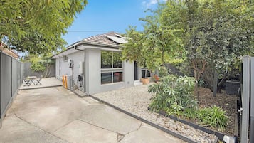 A residential property with a paved driveway, a small patio with outdoor furniture, and a garden area with various plants and trees.