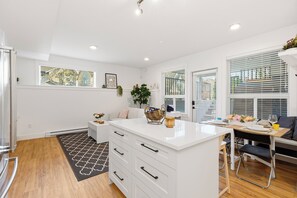 Una cocina moderna con armarios blancos, una isla central y una zona de comedor con mesa y sillas.