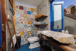 A bathroom with a tiled wall, a toilet, a sink with a stone basin, and a shelf with towels. - Loft House 2BR An Bang Beach Hoi An by Beachside Boutique Homes (Đà Nẵng)