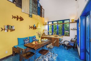 A compact kitchen with a dining area, featuring a wooden table, chairs, and a blue sofa with cushions. - Loft House 2BR An Bang Beach Hoi An by Beachside Boutique Homes (Đà Nẵng)