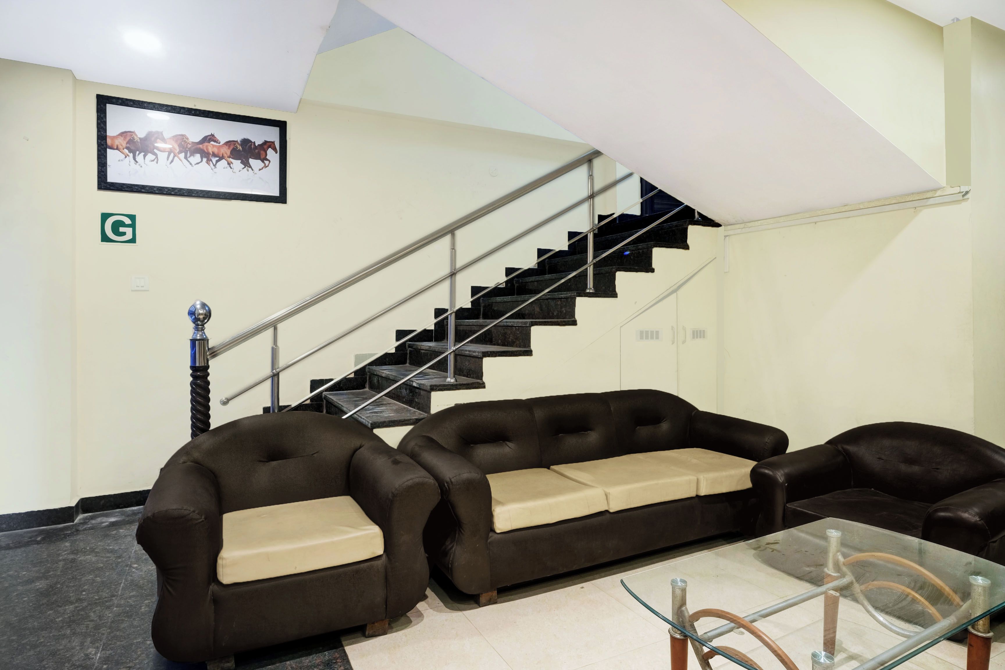 Vestíbulo de hotel con una escalera, un cuadro enmarcado de caballos y una zona de estar con dos sofás y una mesa de vidrio.