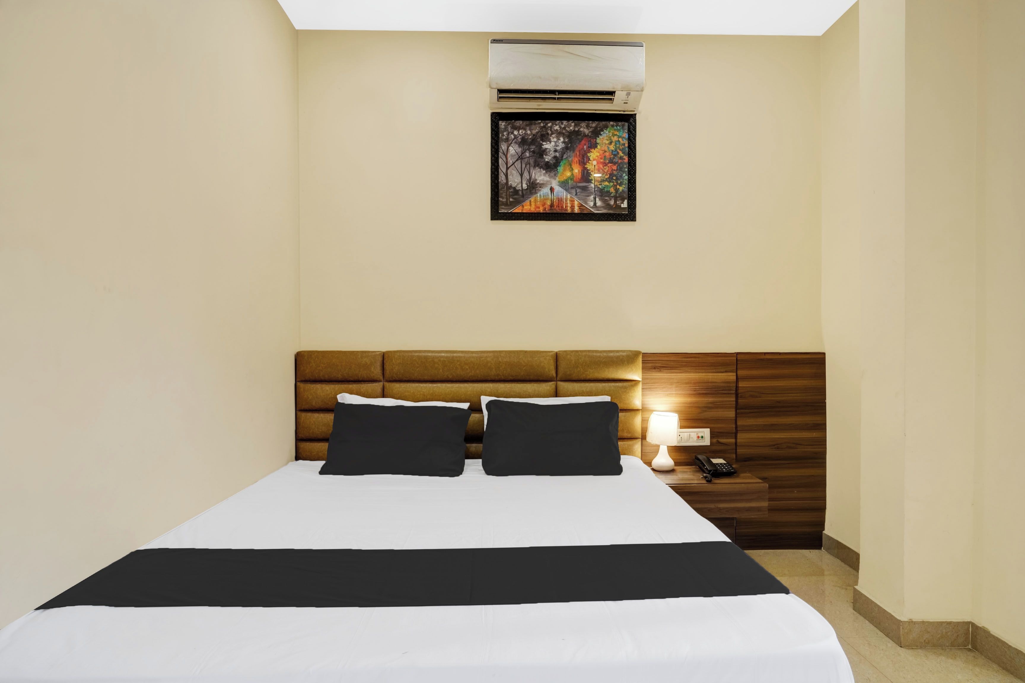 Habitació d'hotel amb un llit, una tauleta de nit, una làmpada i un aparell d'aire condicionat.