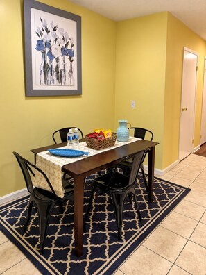 A dining area with a table set for two, chairs, a vase, a basket of snacks, and a framed artwork on the wall. - Hidden Gem! Stylish 2BR Minutes from Dublin (Dublin)