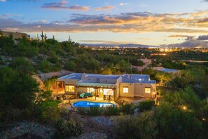 A modern house with a swimming pool, surrounded by greenery and overlooking a cityscape at dusk. - Desert Hilltop Oasis in Foothills Epic (Tucson)