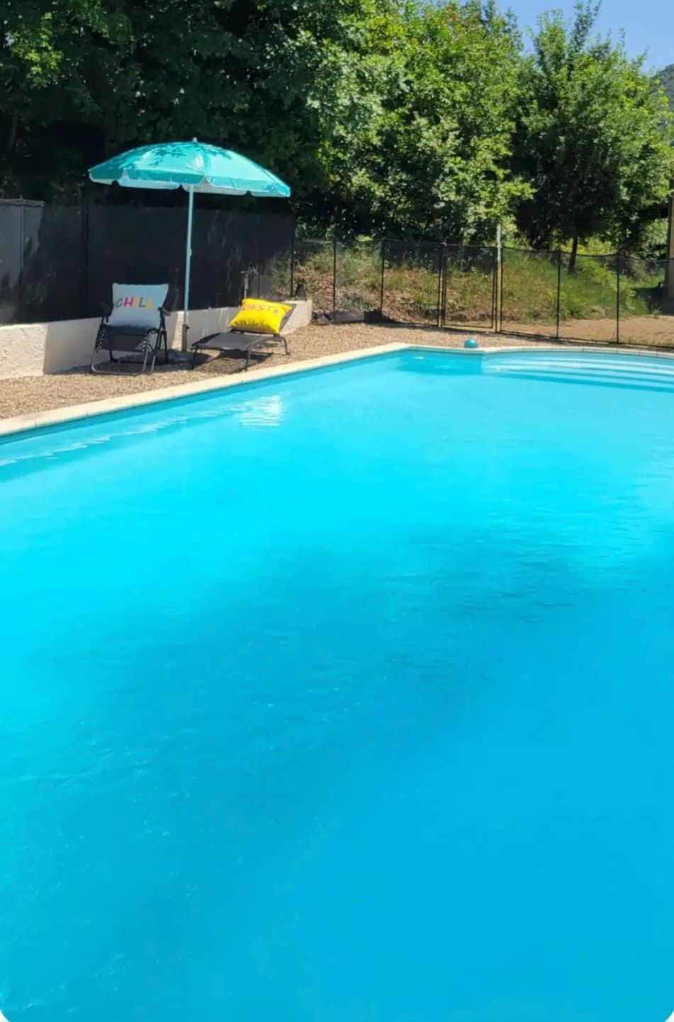 Una piscina con acqua cristallina e azzurra, circondata da lettini e un ombrellone.