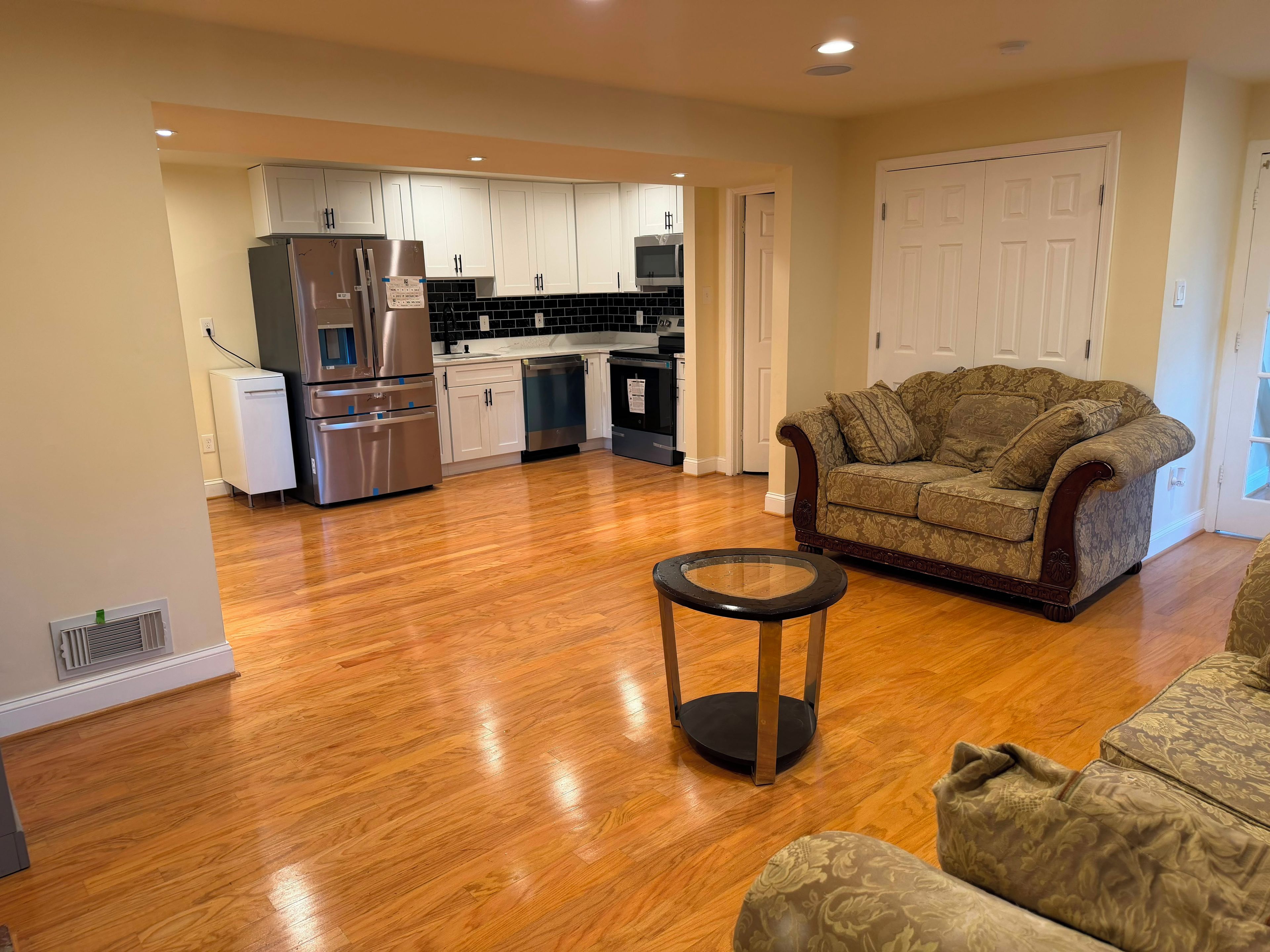 A modern kitchen with stainless steel appliances, a dining area with a patterned sofa, and hardwood flooring.