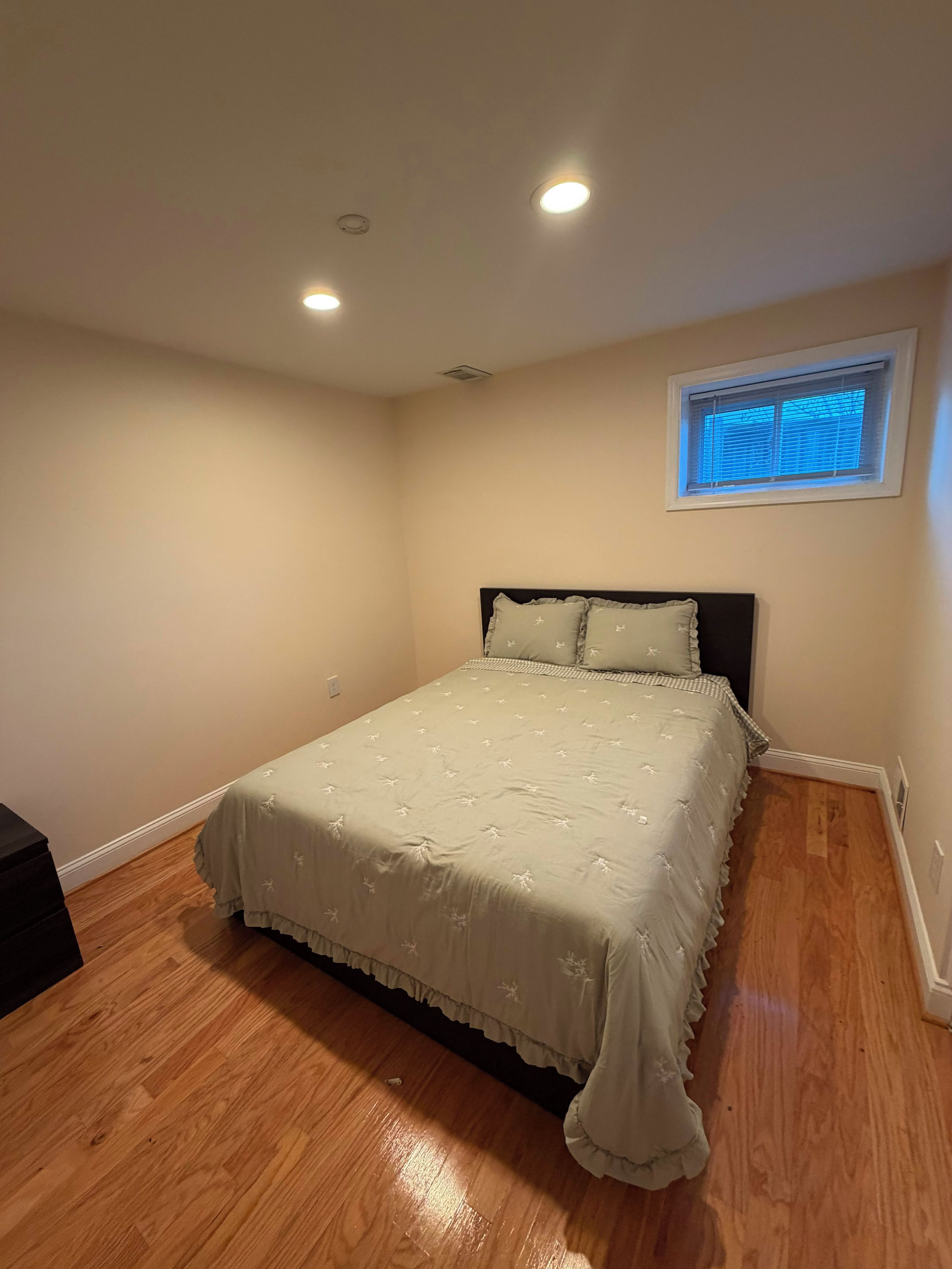 Une chambre à coucher avec un lit, une fenêtre avec des stores et un luminaire au plafond.