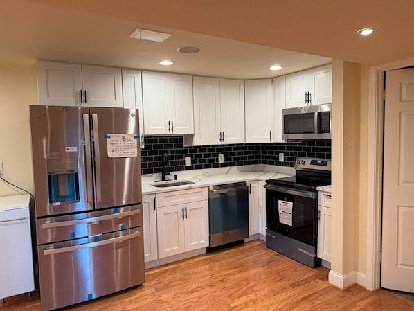 A kitchen with white cabinets, a stainless steel refrigerator, a microwave, and a dishwasher.
