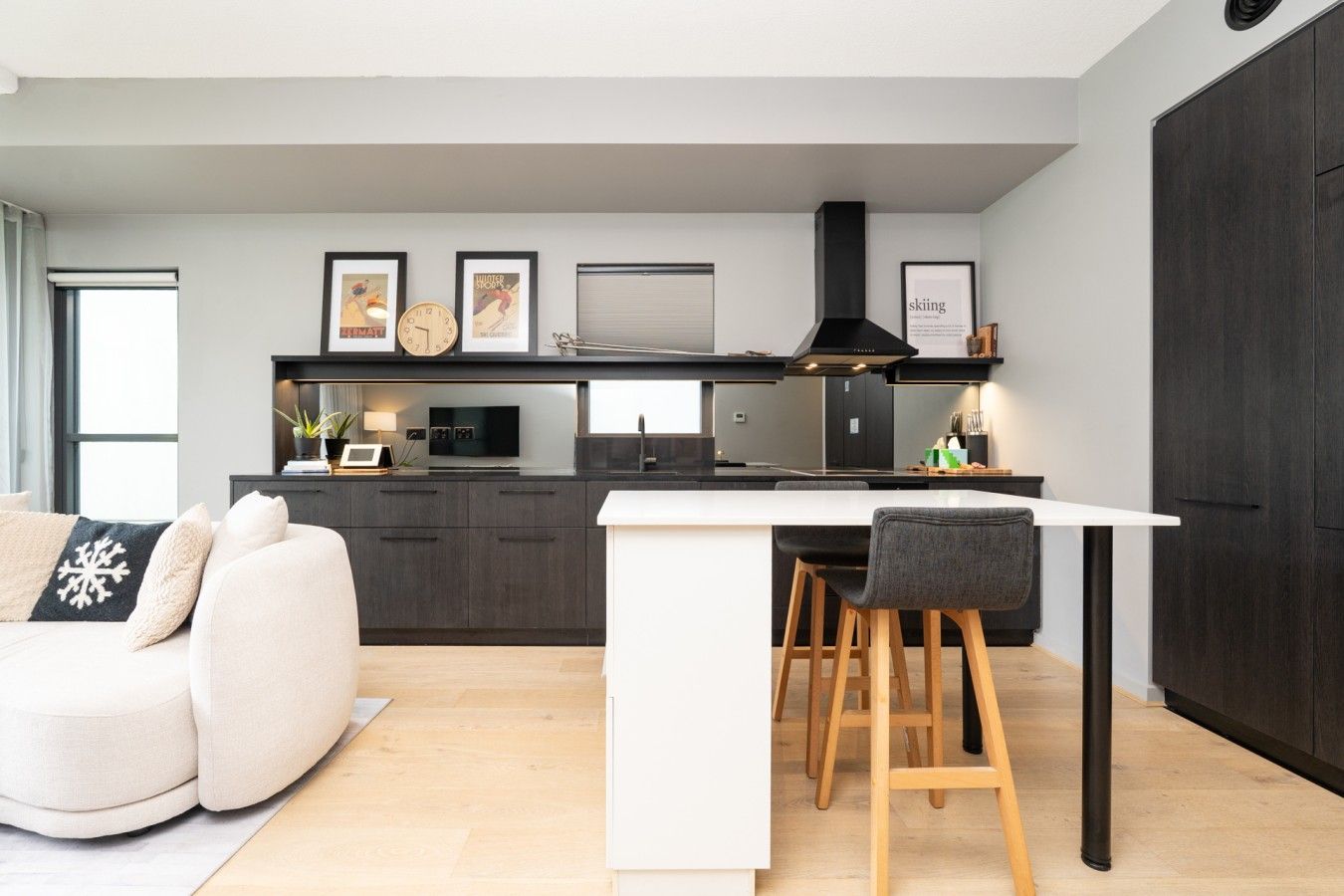 A modern kitchen with a central island, dark cabinetry, and a dining area with a white table and bar stools.