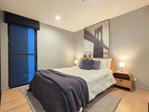 A bedroom with a bed, a nightstand, a lamp, a window with a view, and a door. - Kingston 1BR in a Central Foreshore Location (Canberra (Inner South))