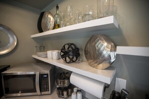A kitchen with a microwave, shelves with glassware, and decorative items. - Wall Street Suites 3 | Queen Studio near SIU with Kitchen (Carbondale)
